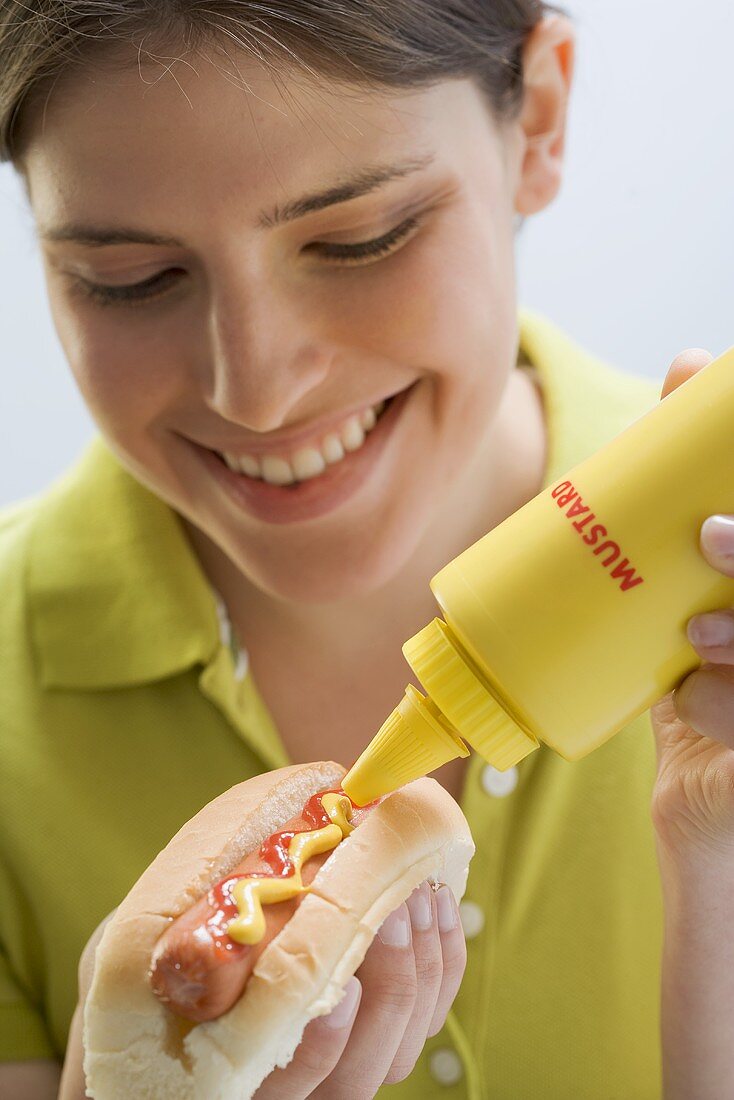 Young woman putting mustard on hot dog