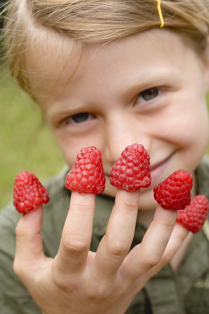 Mädchen mit Himbeeren auf den Fingern