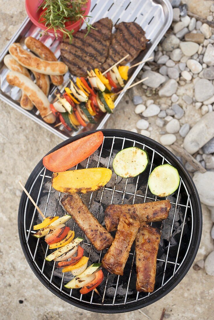 Meat, sausages and vegetables on barbecue and in dish