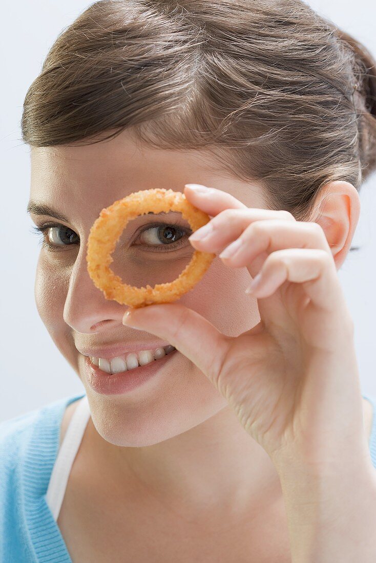 Young woman looking through deep-fried onion ring