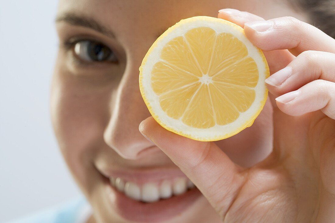 Young woman holding lemon in front of her eye