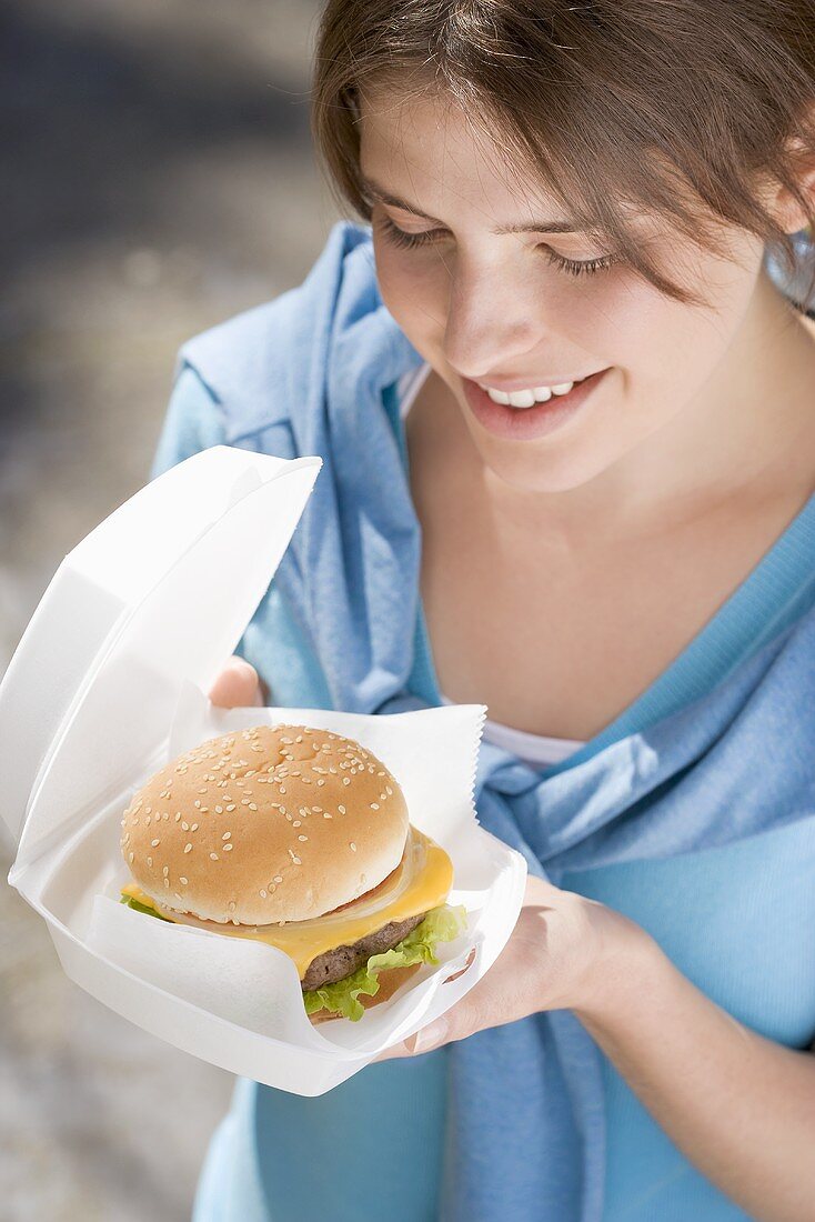 Young woman with cheeseburger out of doors