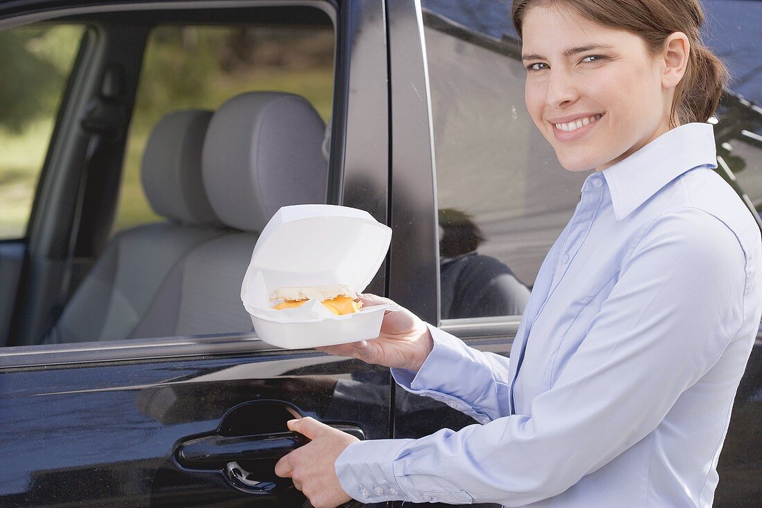 Junge Frau trägt English Muffin in Styroporschachtel zum Auto