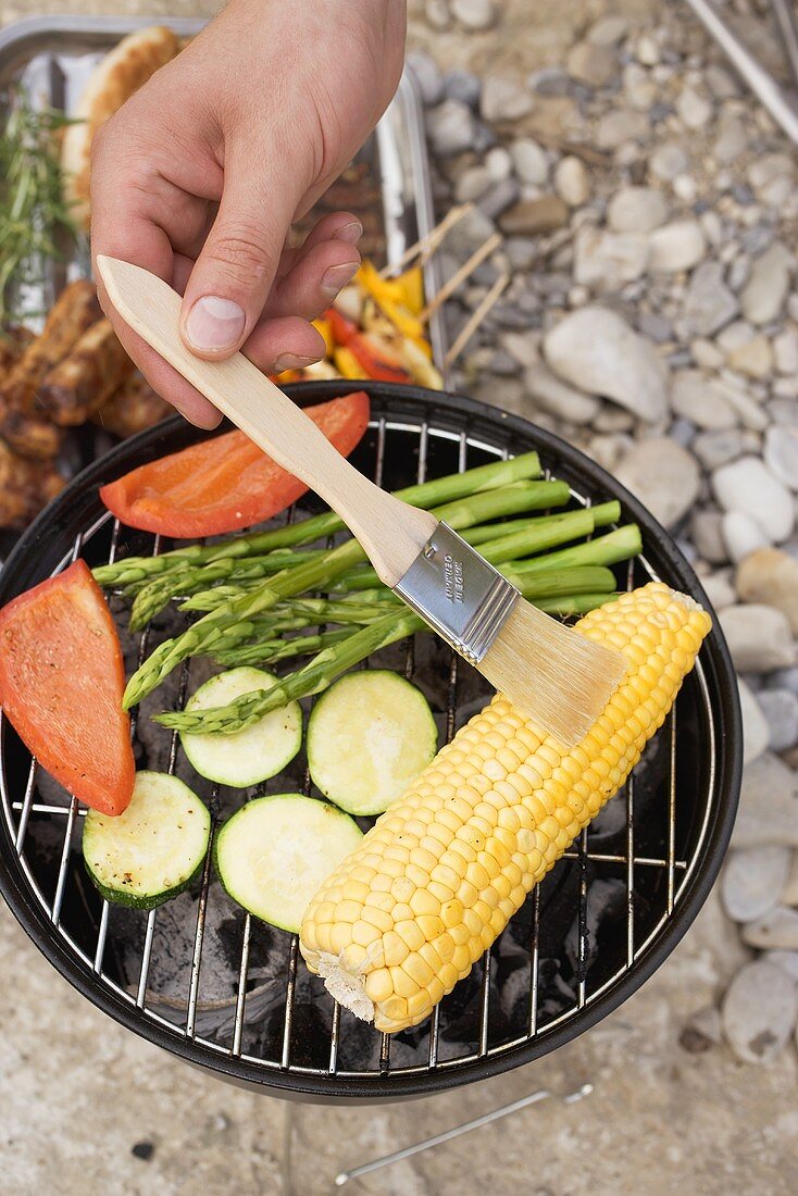 Hand brushing corn cob on barbecue with oil