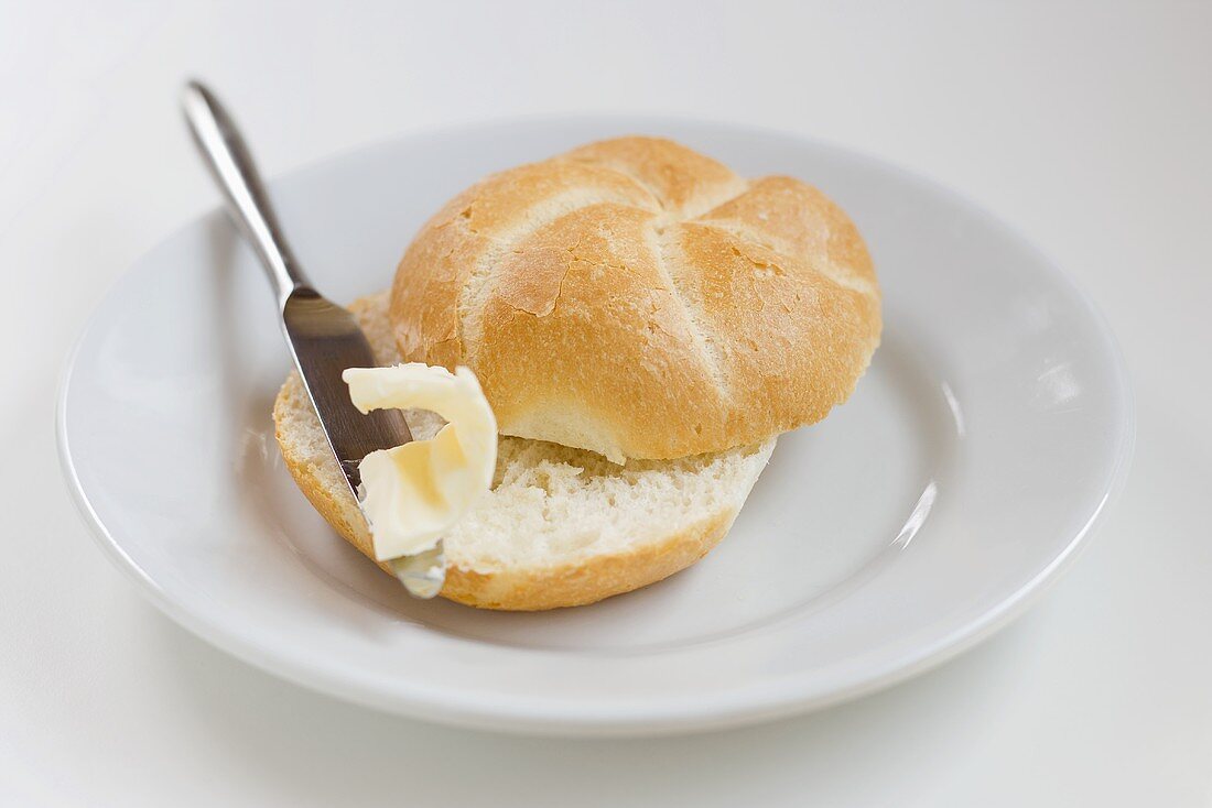 Bread roll with butter and knife on plate