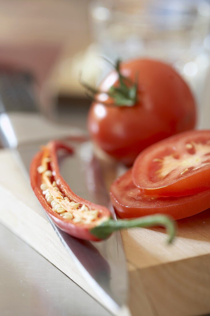 Tomaten und halbe Chilischote auf Schneidebrett mit Messer
