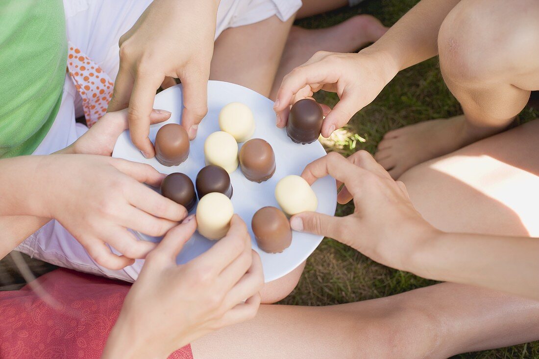 Children's hands reaching for chocolate-coated marshmallows