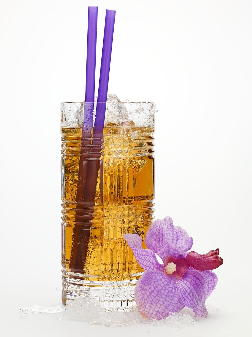 Rum drink with ice cubes and straws, orchid beside it
