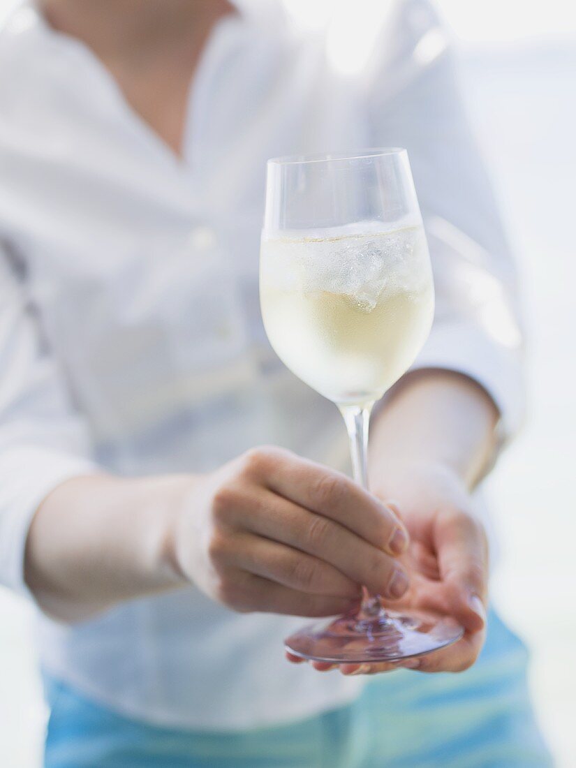 Frau hält Glas Weißwein mit Eiswürfeln im Freien