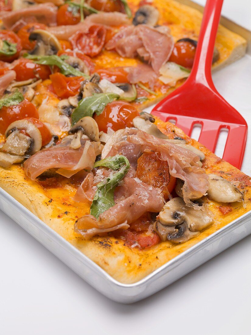 Pizza topped with ham, tomatoes, mushrooms and rocket