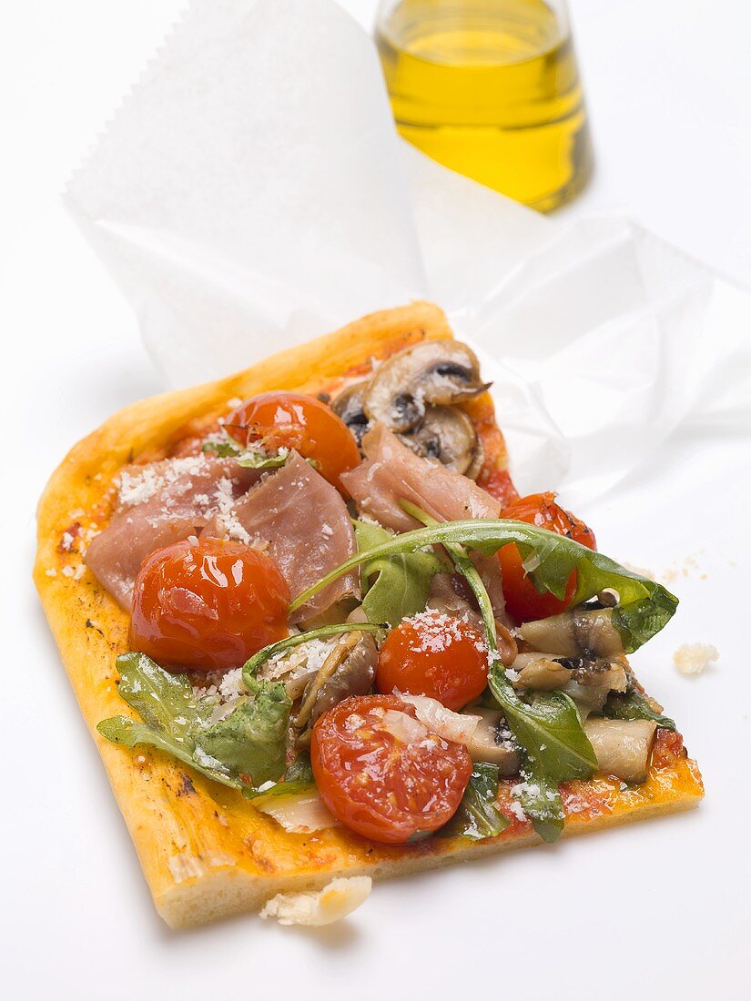 Slice of pizza topped with ham, tomatoes, mushrooms, rocket
