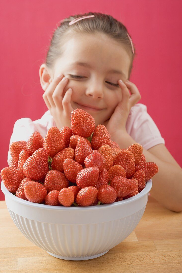 Kleines Mädchen sitzt verträumt bei einer Schüssel Erdbeeren
