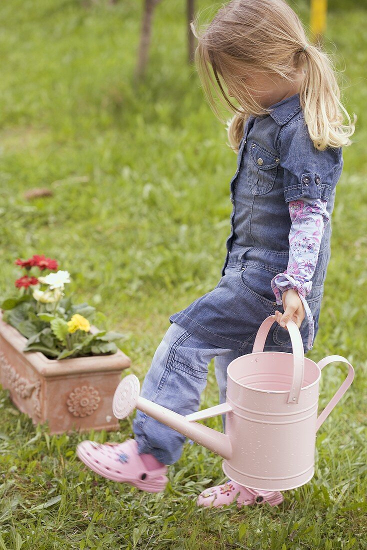 Little girl carrying water can through garden