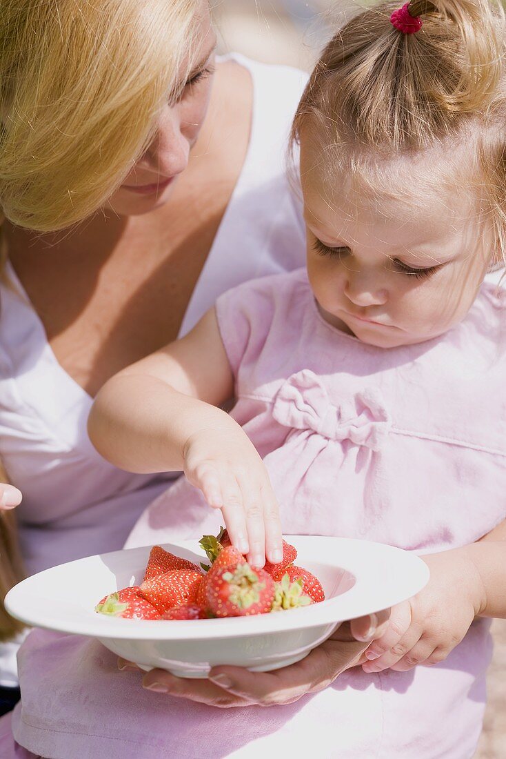 Mutter und kleine Tochter mit einem Teller Erdbeeren