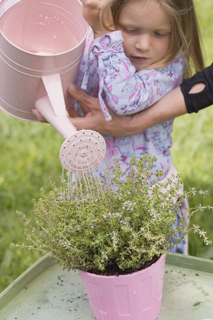 Mother helping daughter to water thyme