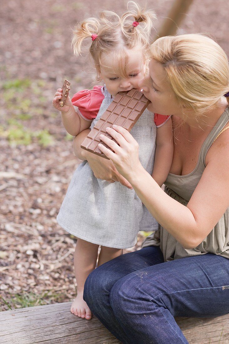 Mother and young daughter biting into a bar of chocolate