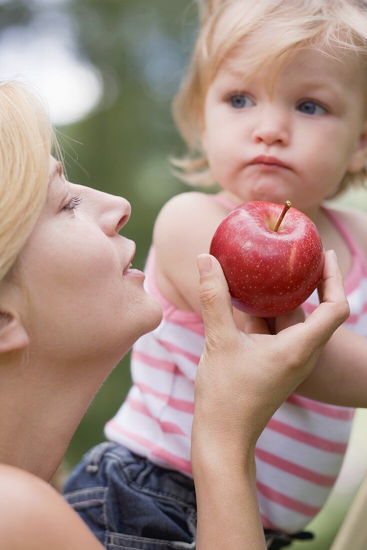 Mother offering young daughter a red apple