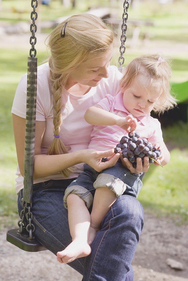 Mutter und kleine Tochter essen Trauben auf einer Schaukel