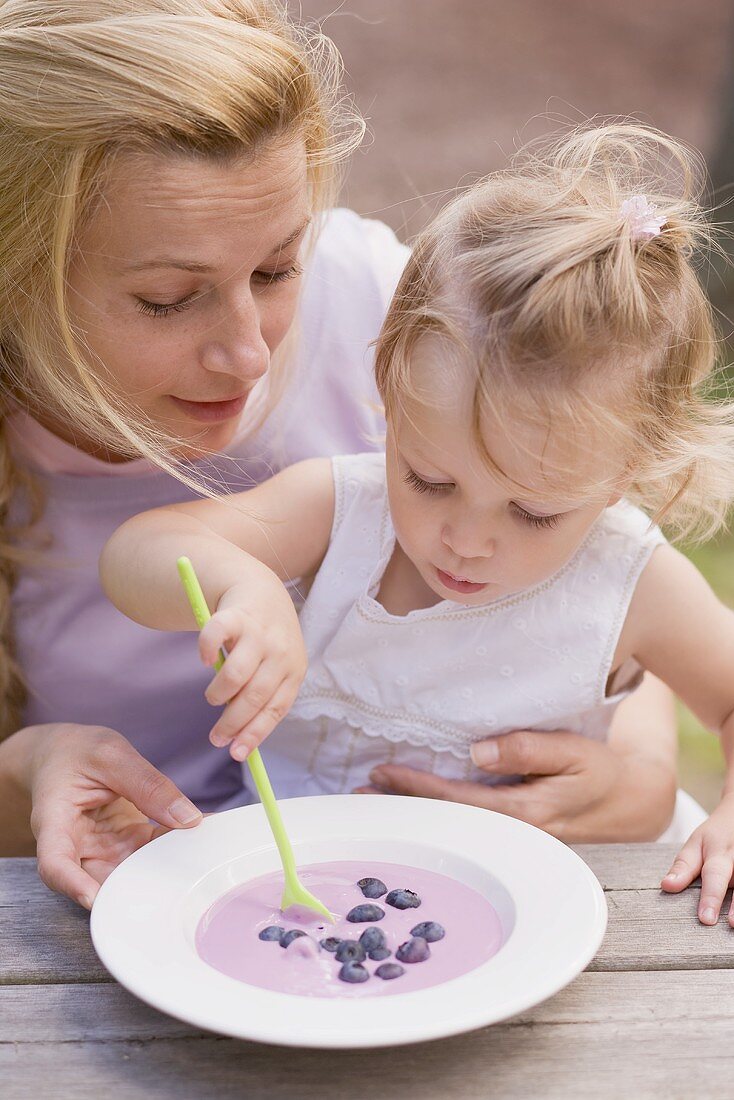 Little girl stirring blueberry yoghurt with spoon