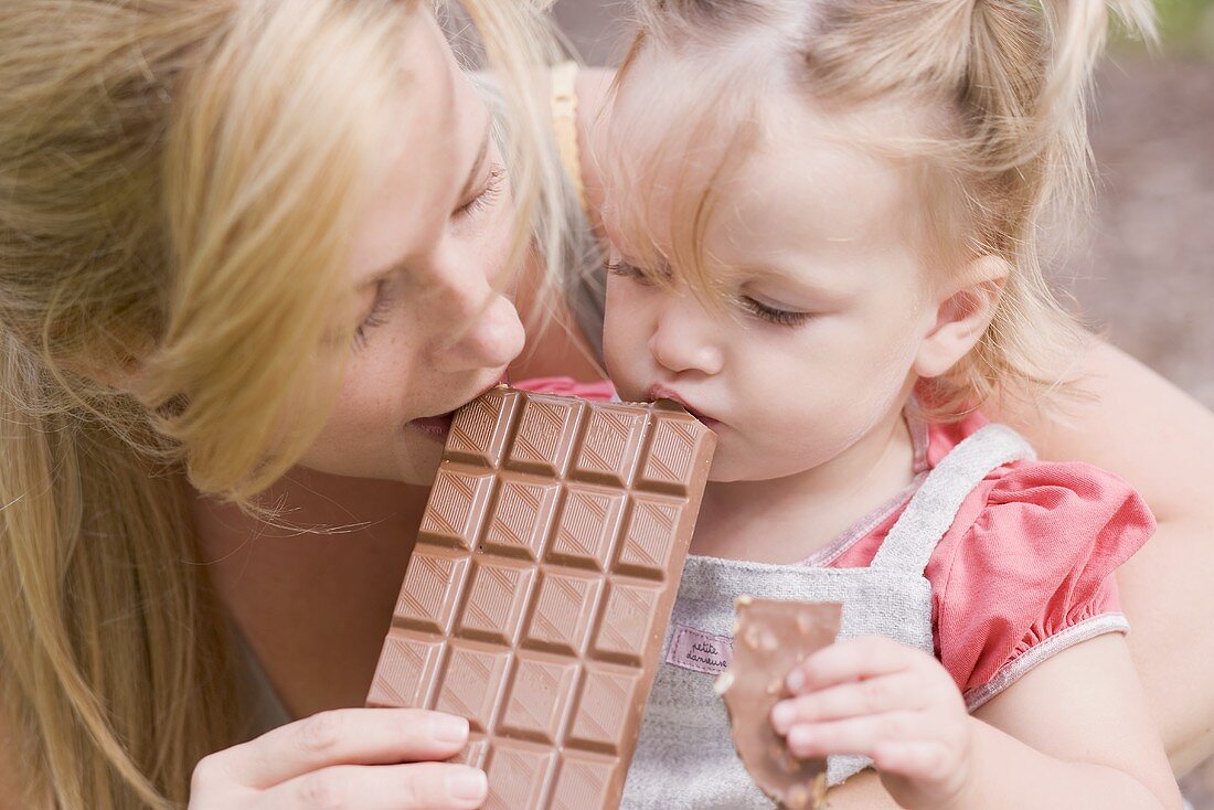 Mother and young daughter biting into a bar of chocolate