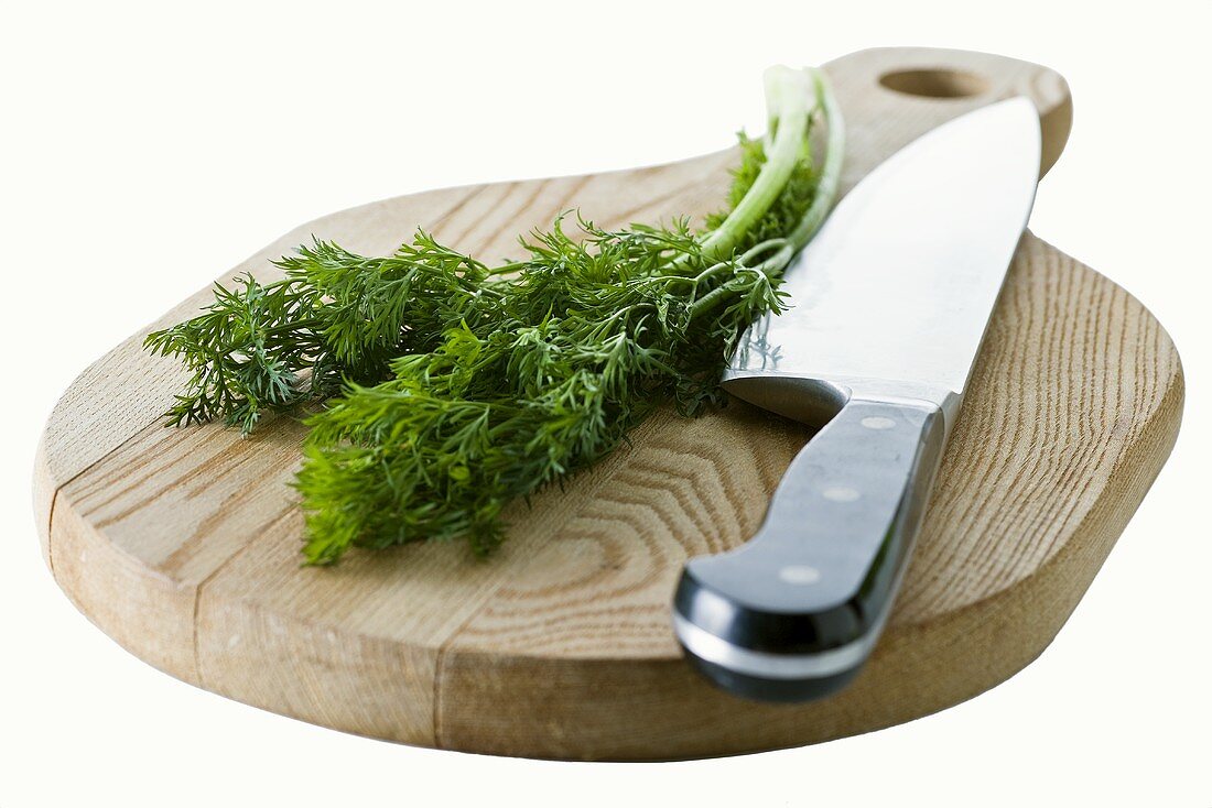 Dill with knife on wooden board