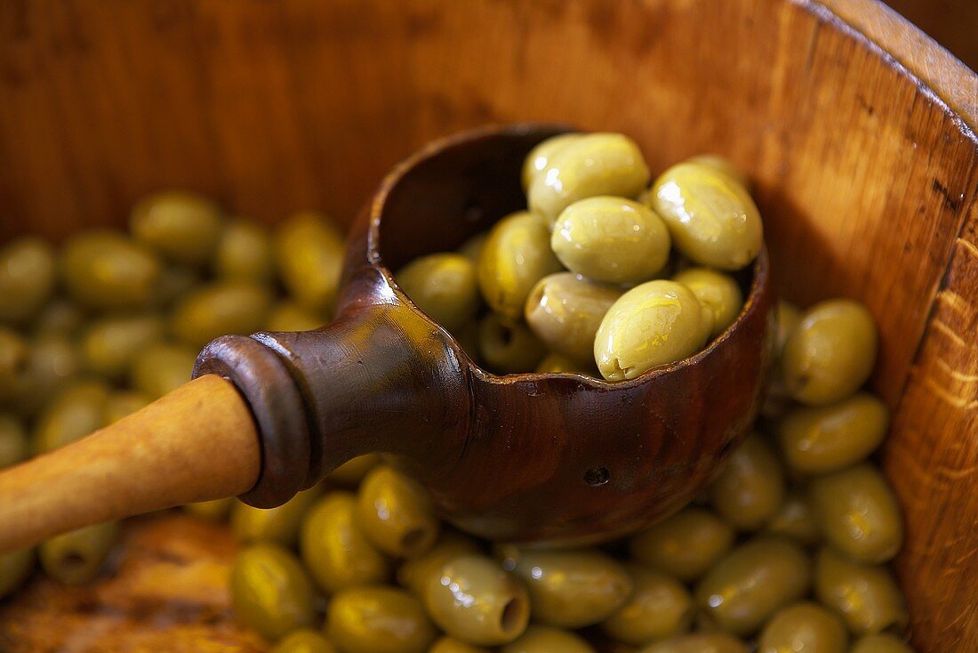 Eingelegte grüne Oliven in Holzfass und Kelle