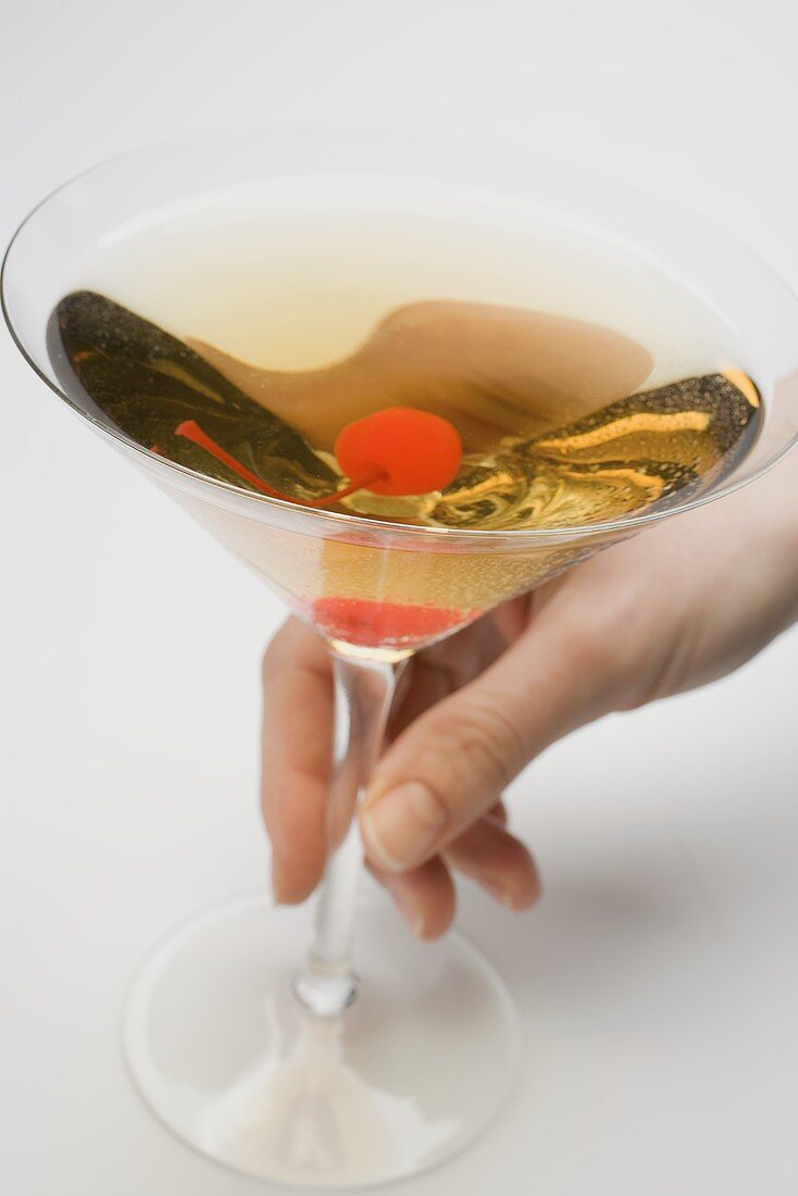Hand holding a glass of Manhattan with cocktail cherry