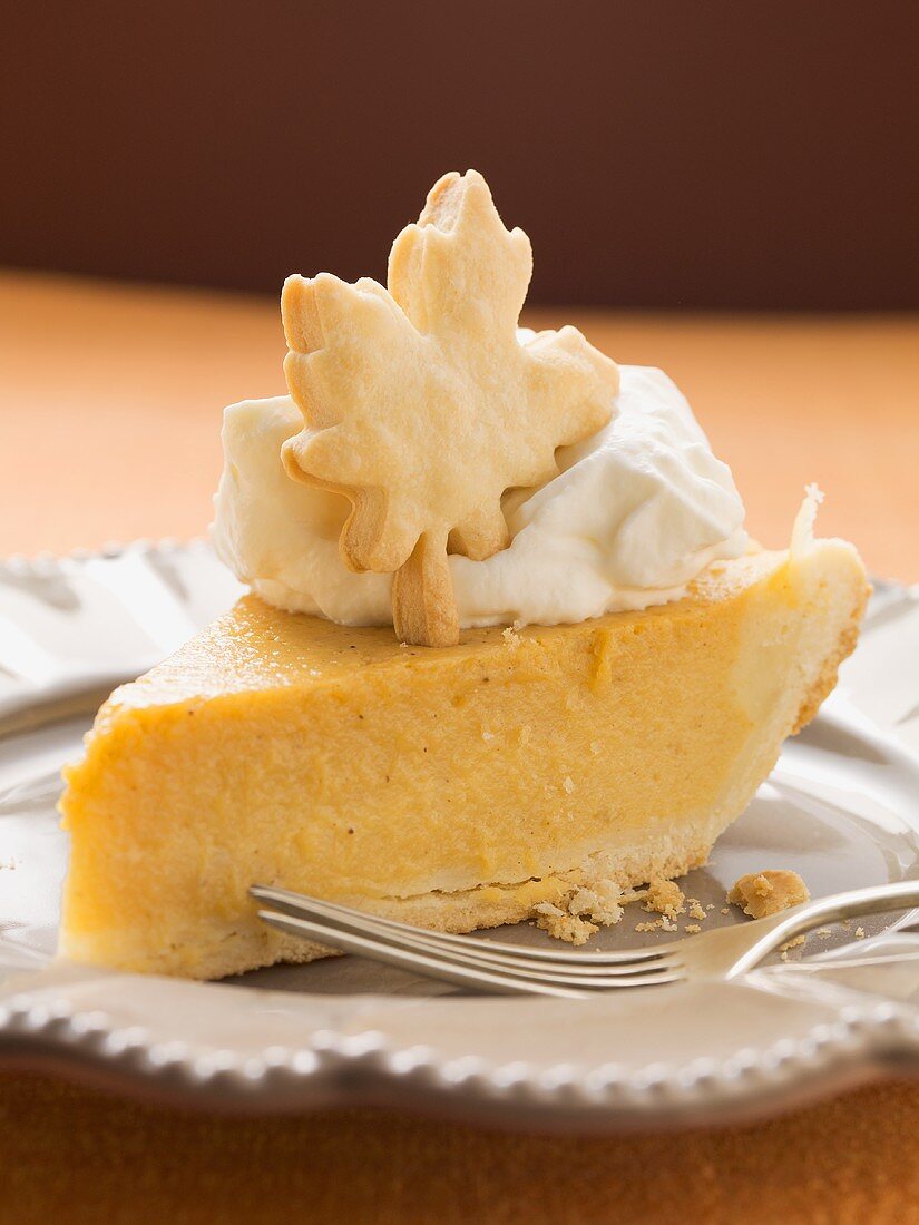 Piece of pumpkin pie with cream and pastry leaf