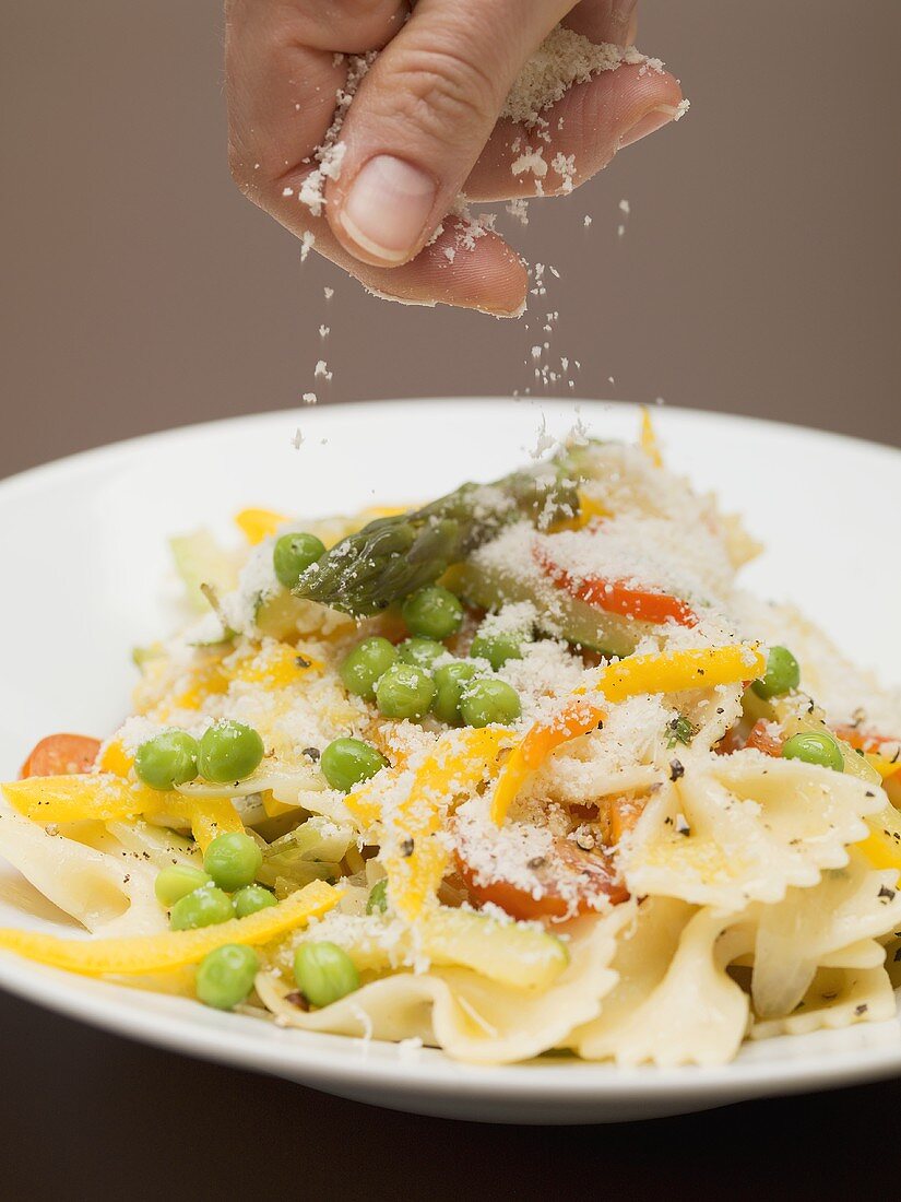 Hand sprinkling cheese on farfalle with vegetables