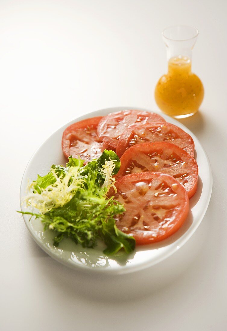 Tomatenscheiben und Frisée auf einem Teller mit Dressing