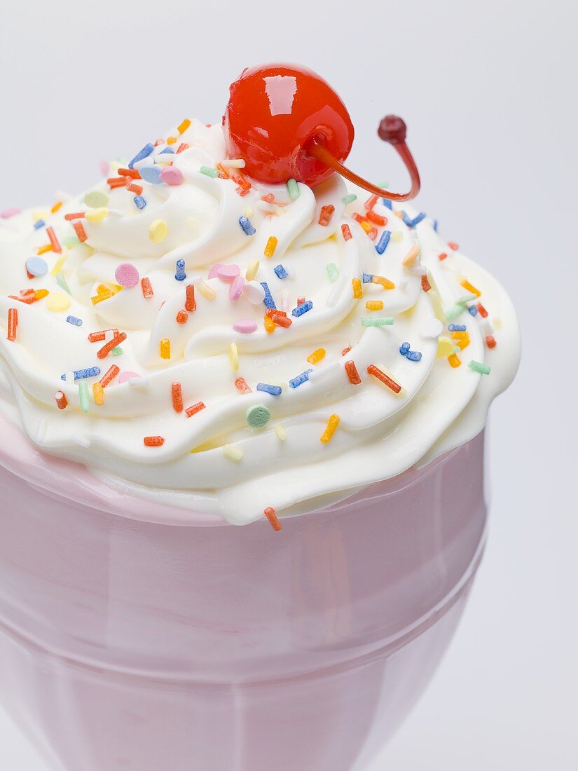 Milkshake with cream, sprinkles & cocktail cherry (close-up)