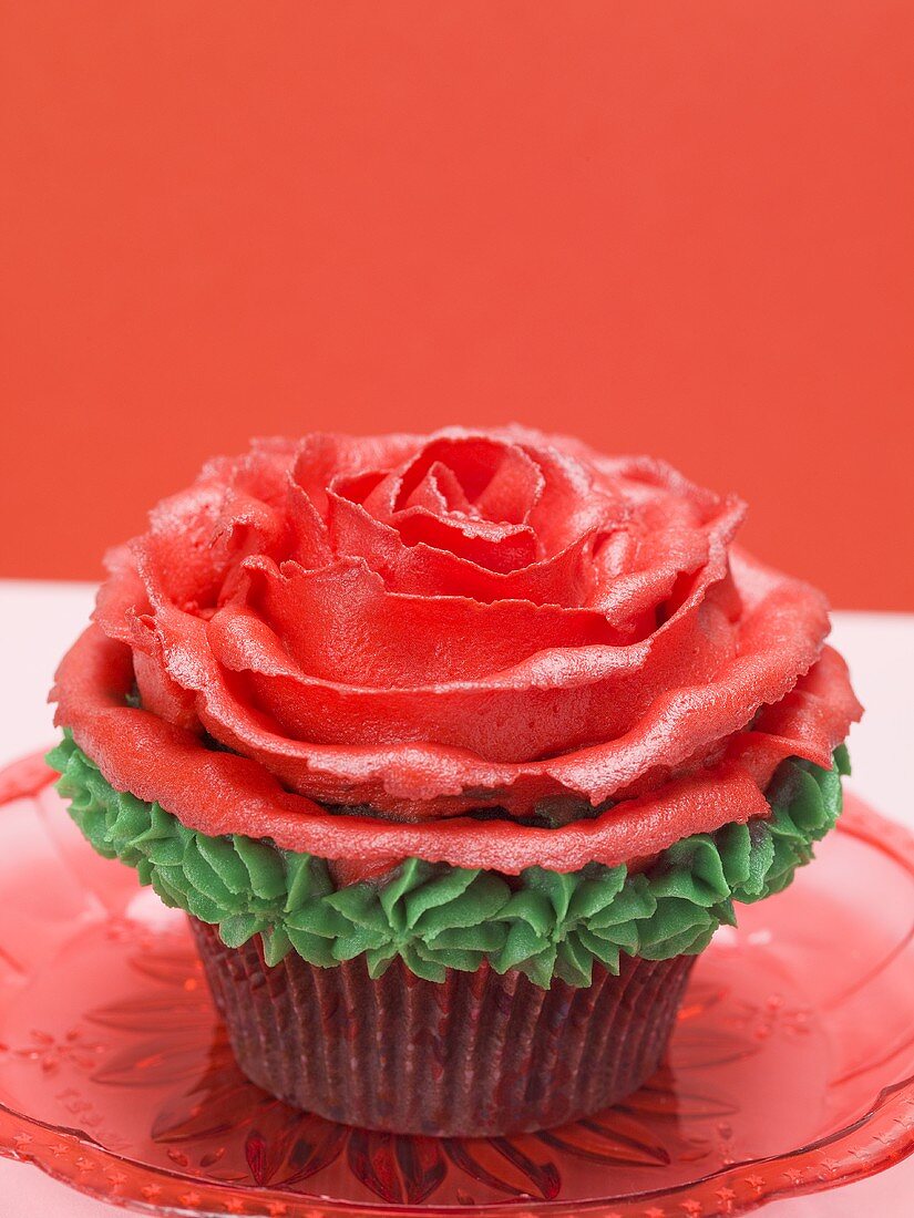 Cupcake with red marzipan rose against red background