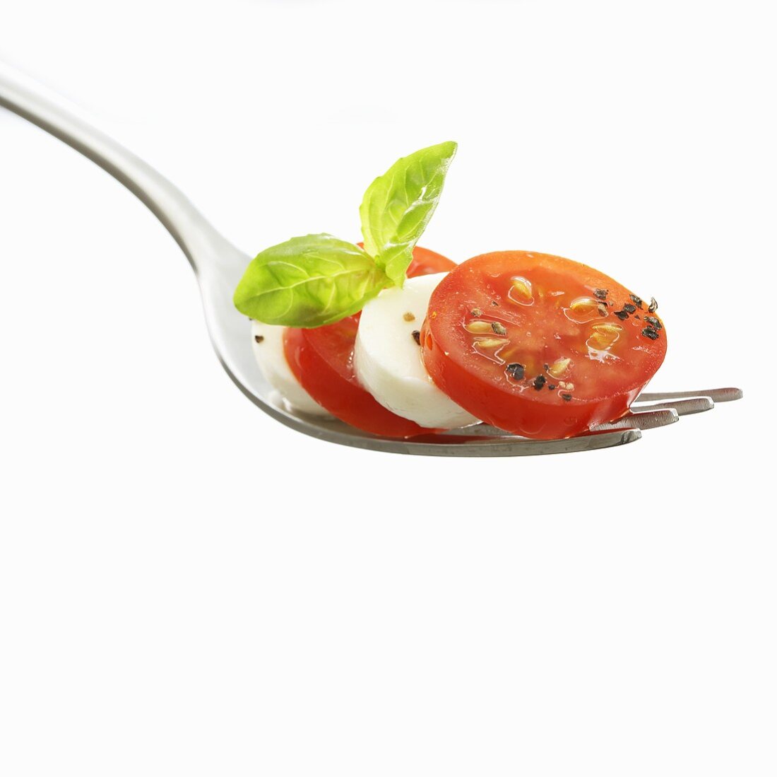 Tomato slices with mozzarella and basil on fork