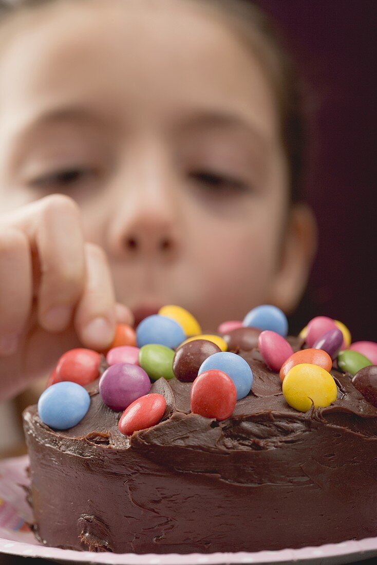 Little girl taking chocolate bean from birthday cake