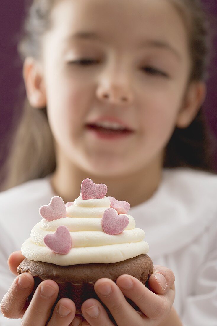 Kleines Mädchen hält Cupcake mit Zuckerherzen