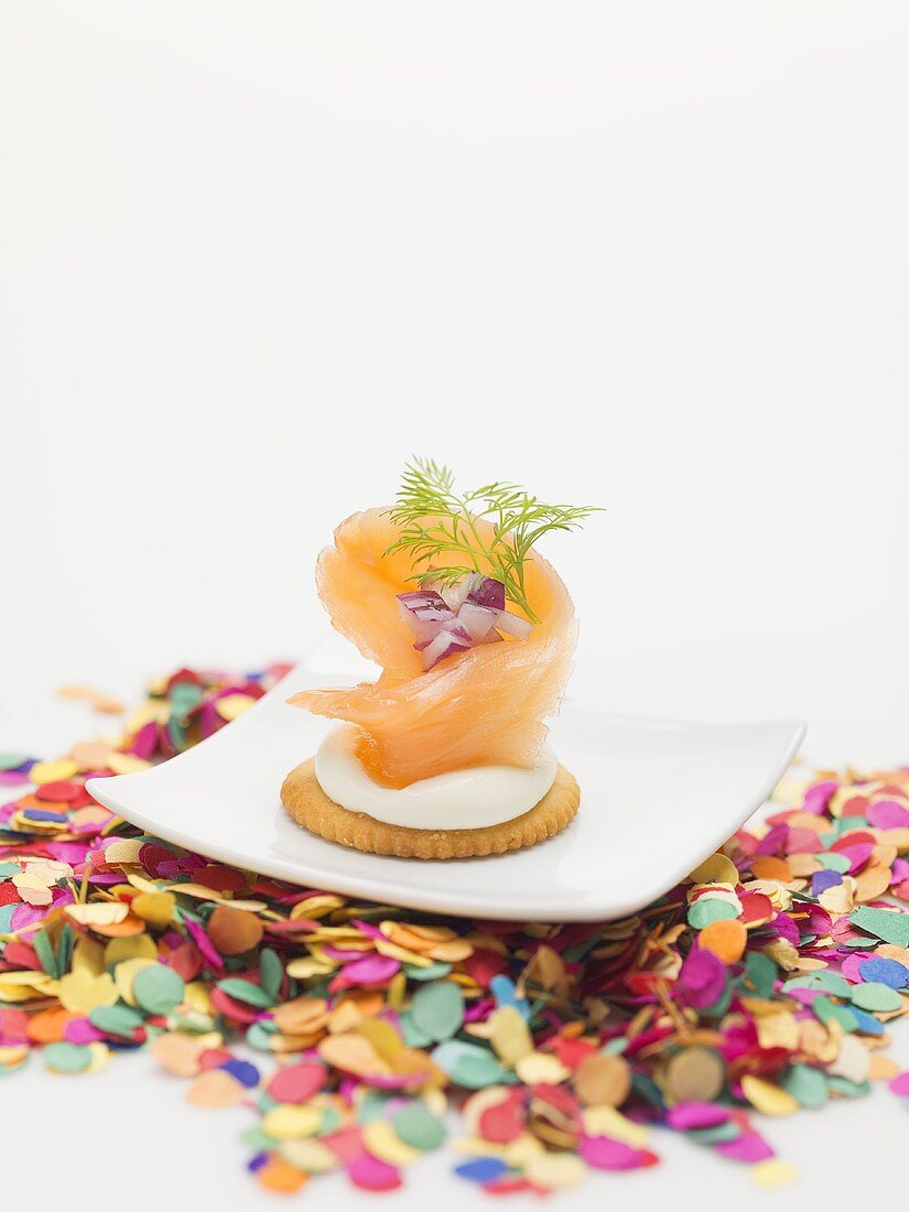 Smoked salmon on cracker on plate surrounded by confetti