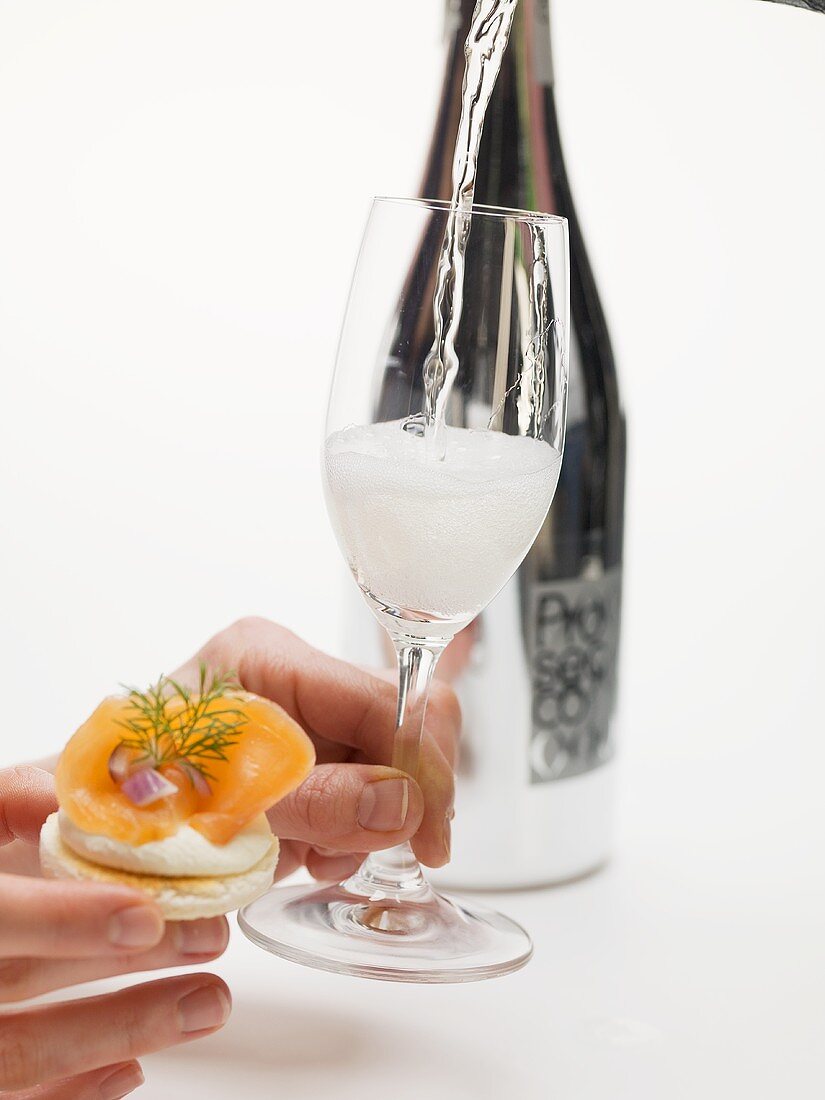 Hands holding cracker with smoked salmon & glass of Prosecco