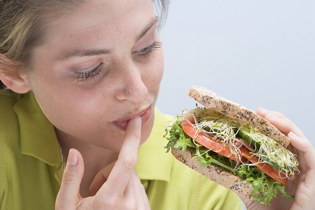 Young woman holding sandwich and licking her finger