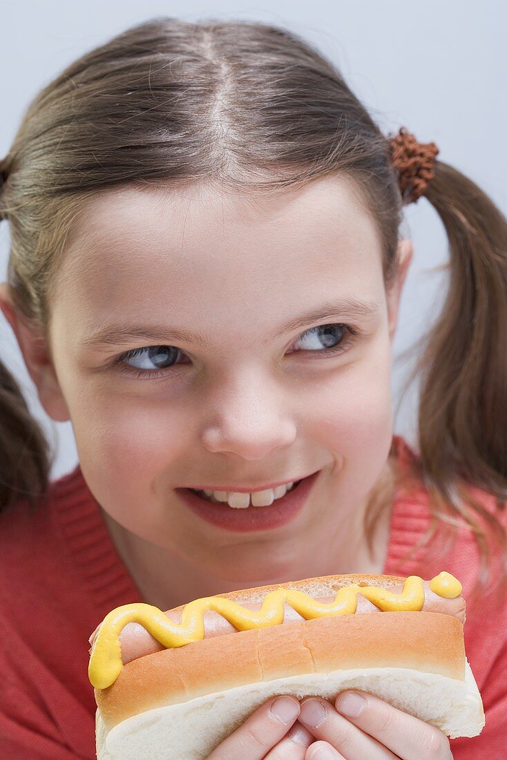 Smiling girl holding hot dog with mustard