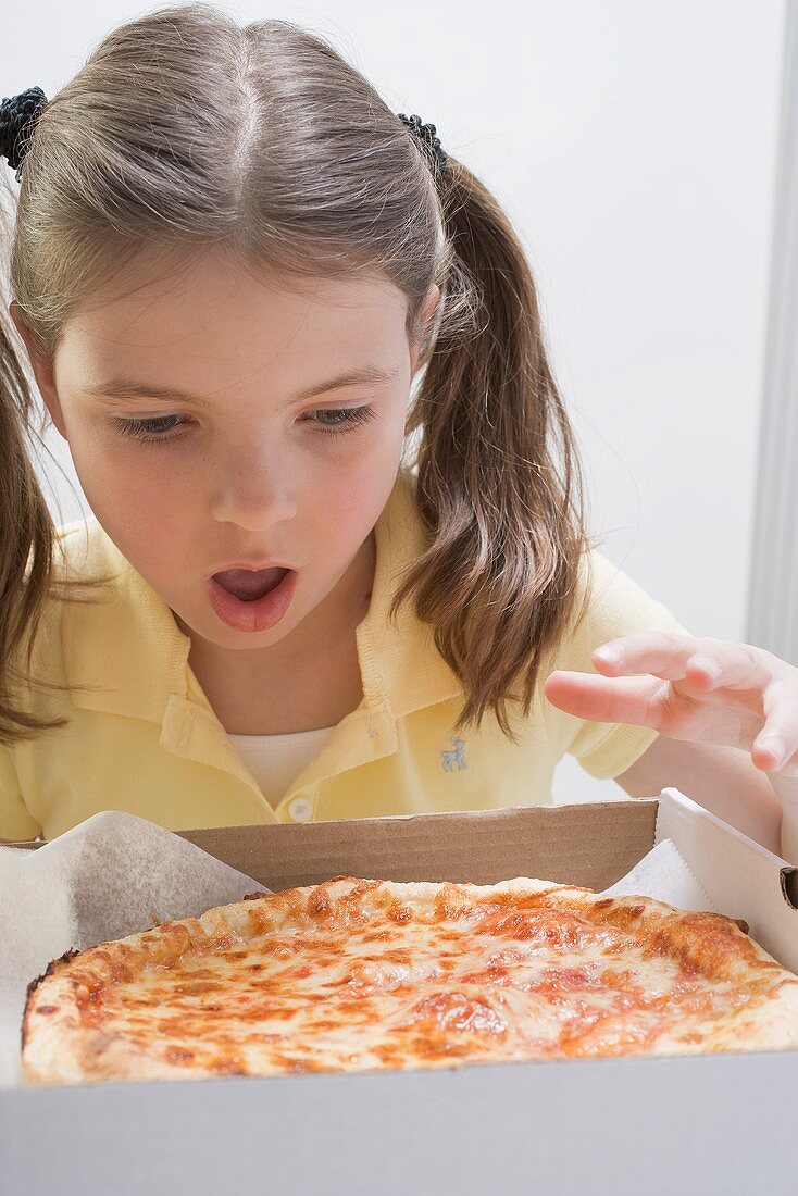 Mädchen blickt staunend auf eine frische Pizza in der Schachtel