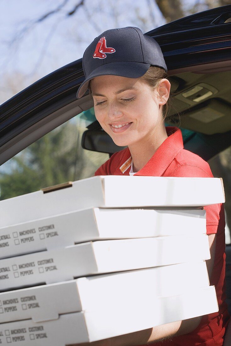 Woman in baseball cap delivering five boxes of fresh pizza