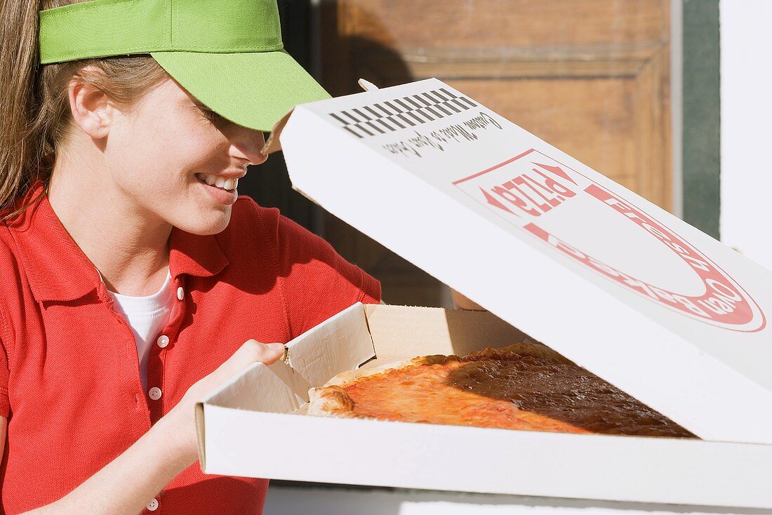 Woman in sun visor looking into opened pizza box