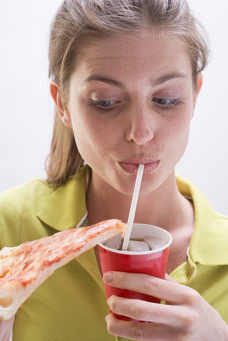 Young woman holding slice of pizza and drinking cola