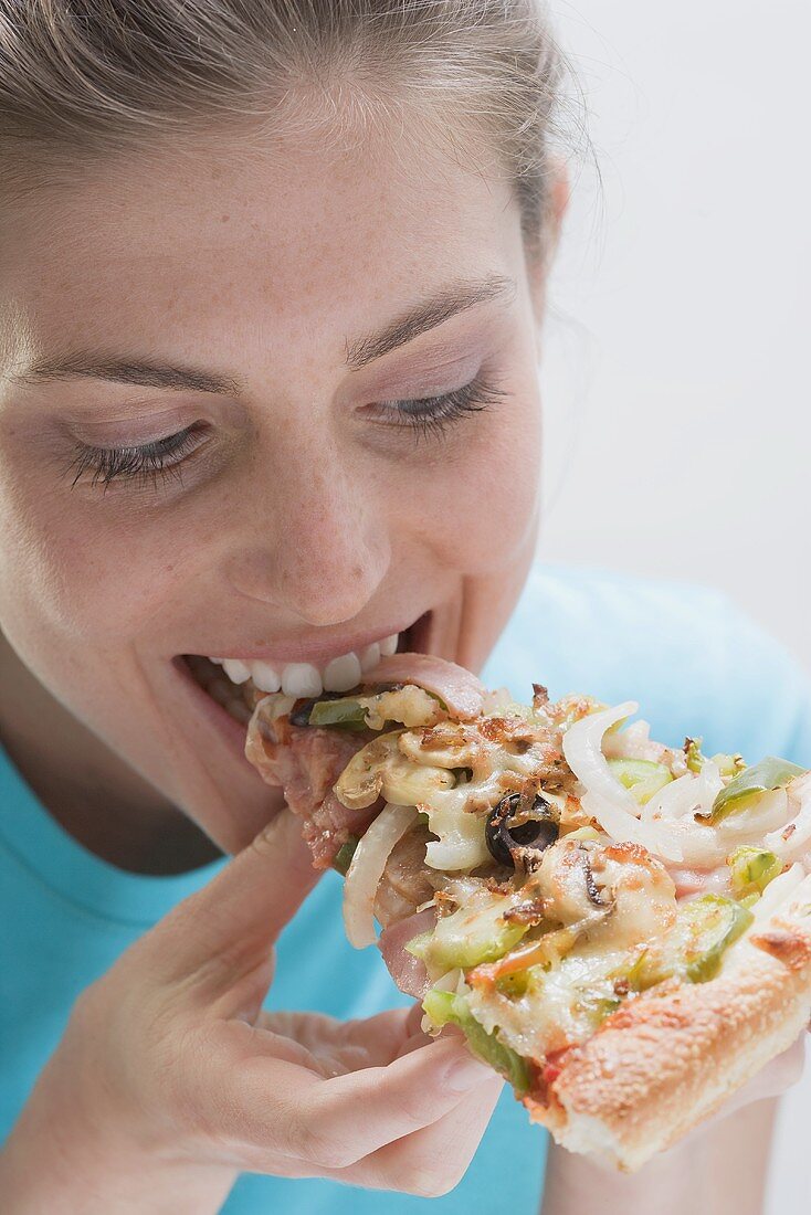 Young woman eating a slice of vegetable pizza