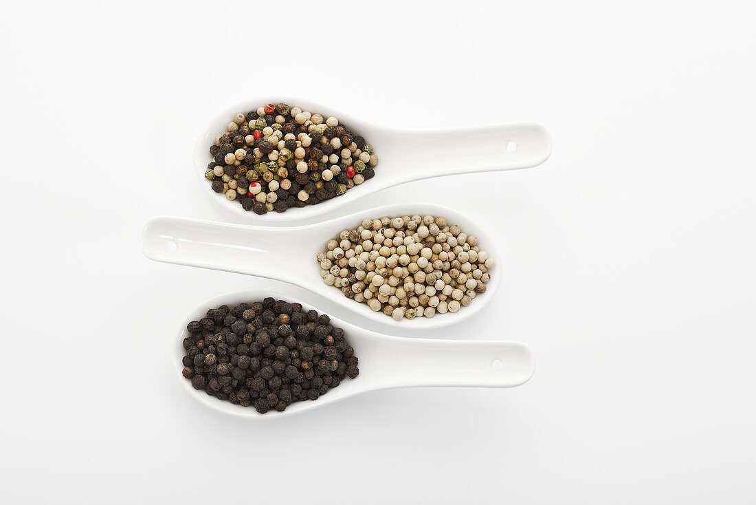 Different types of peppercorns in three spoons (overhead view)