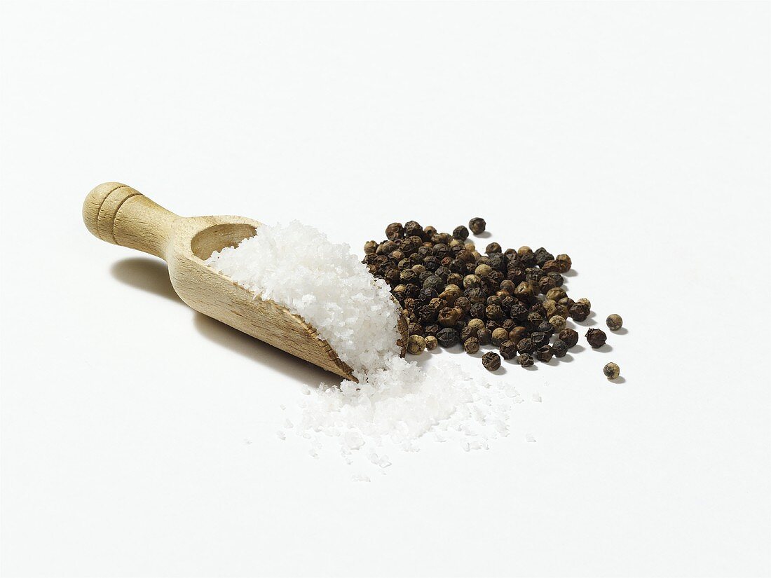 Salt in wooden scoop, peppercorns beside it