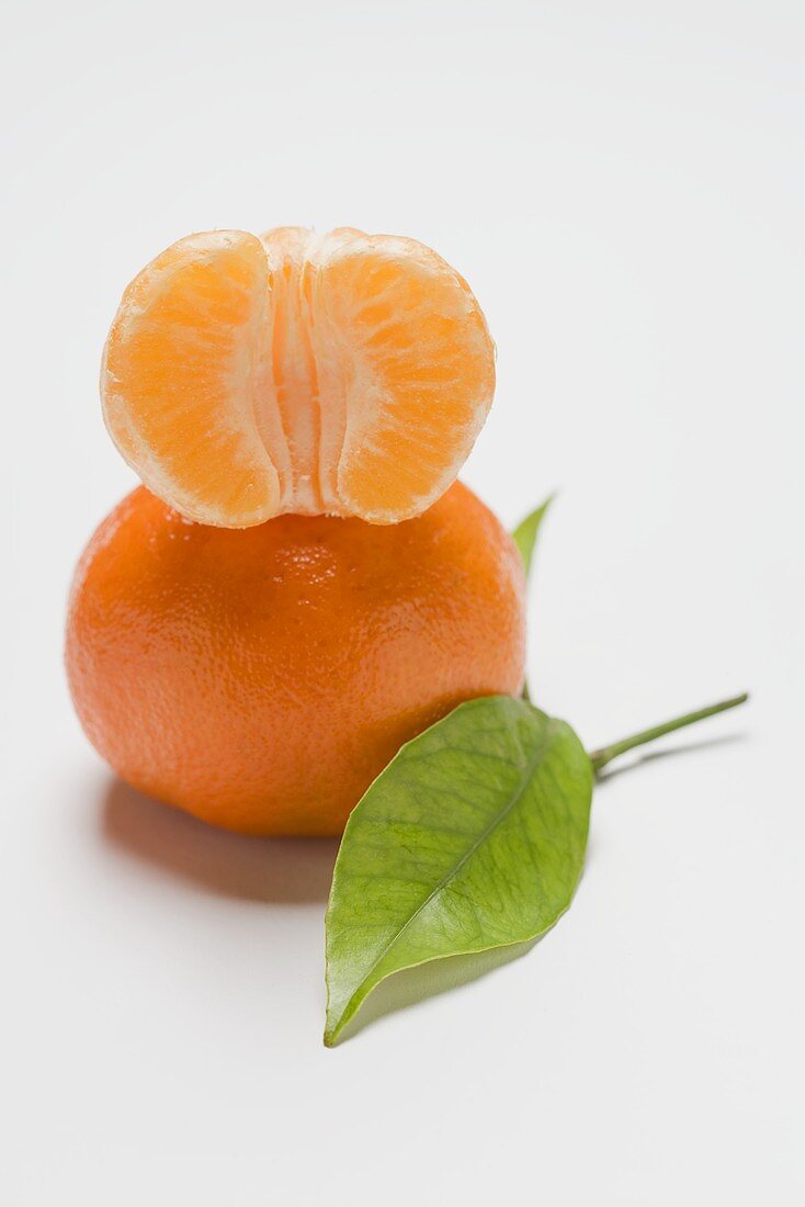 Half of a peeled clementine on unpeeled clementine, leaf
