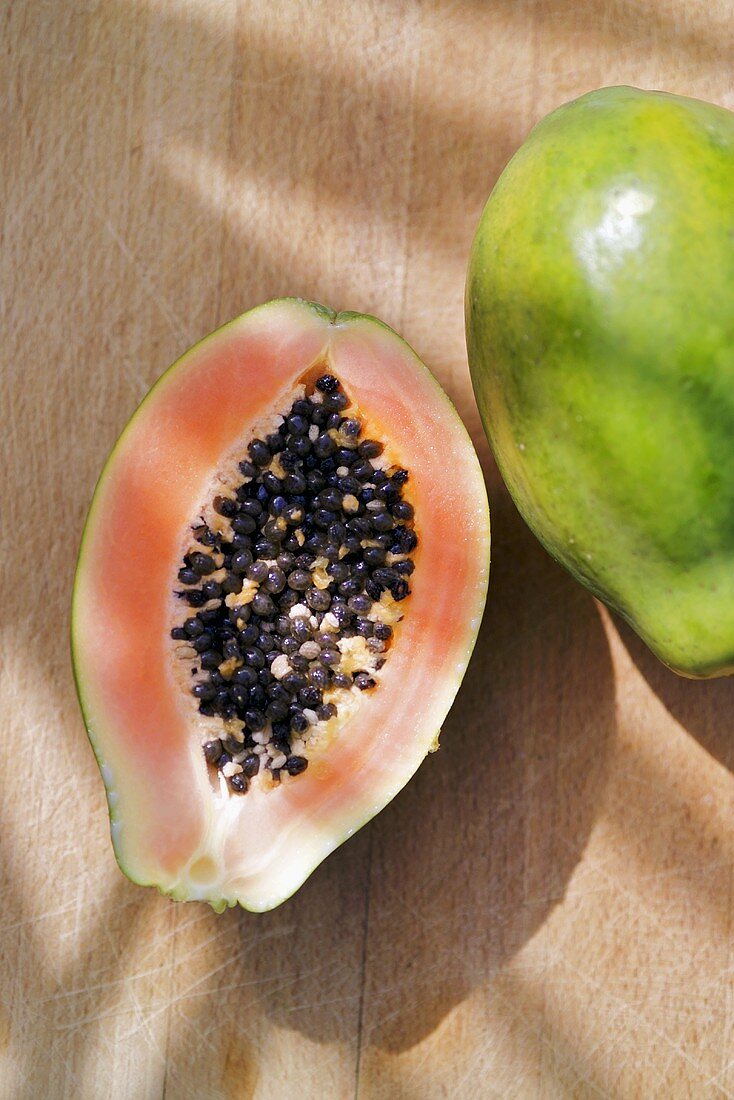 Half a papaya beside a whole papaya (overhead view)