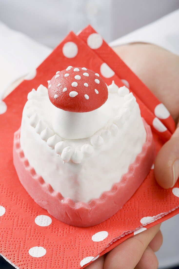 Hands holding small cake with marzipan fly agaric