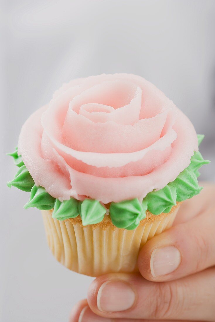Hand holding cupcake with pink marzipan rose